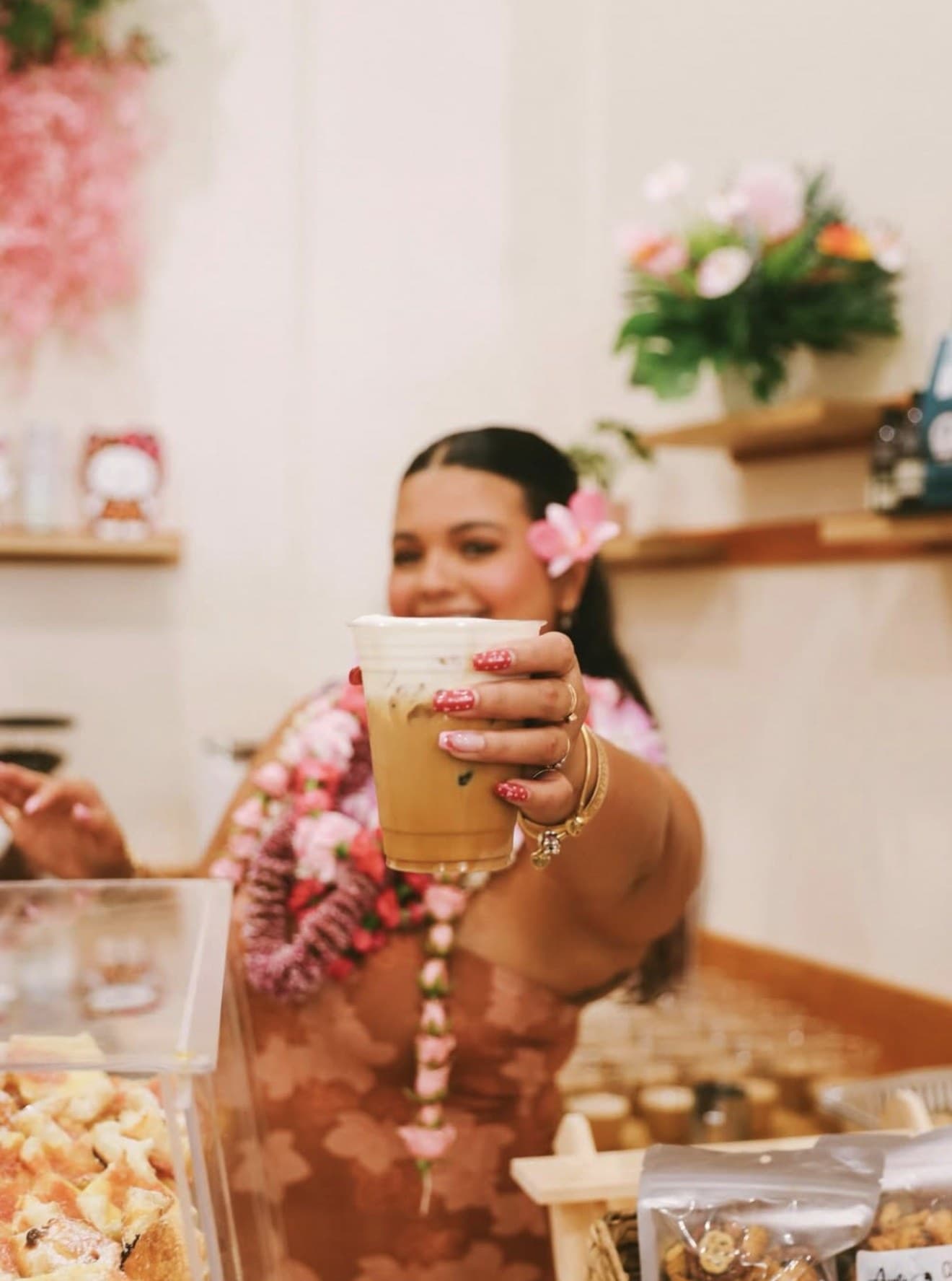 A barista at Sip N' Pretty holding a Wehi Latte, fresh plumeria leis around her neck.